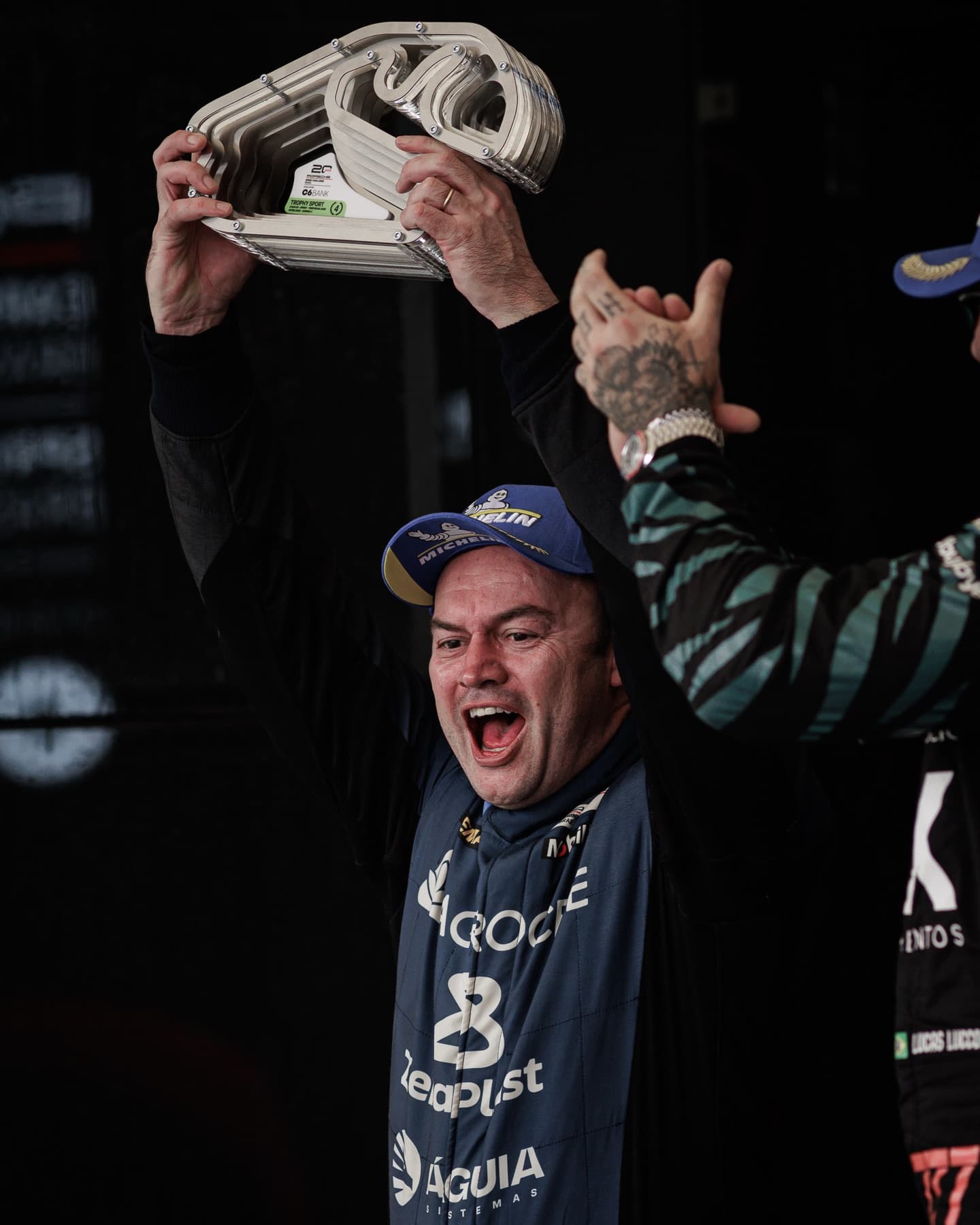 Guilherme Figueiredo comemora no pódio erguendo o troféu, com o macacão da Agrocete Racing e as marcas dos patrocinadores.