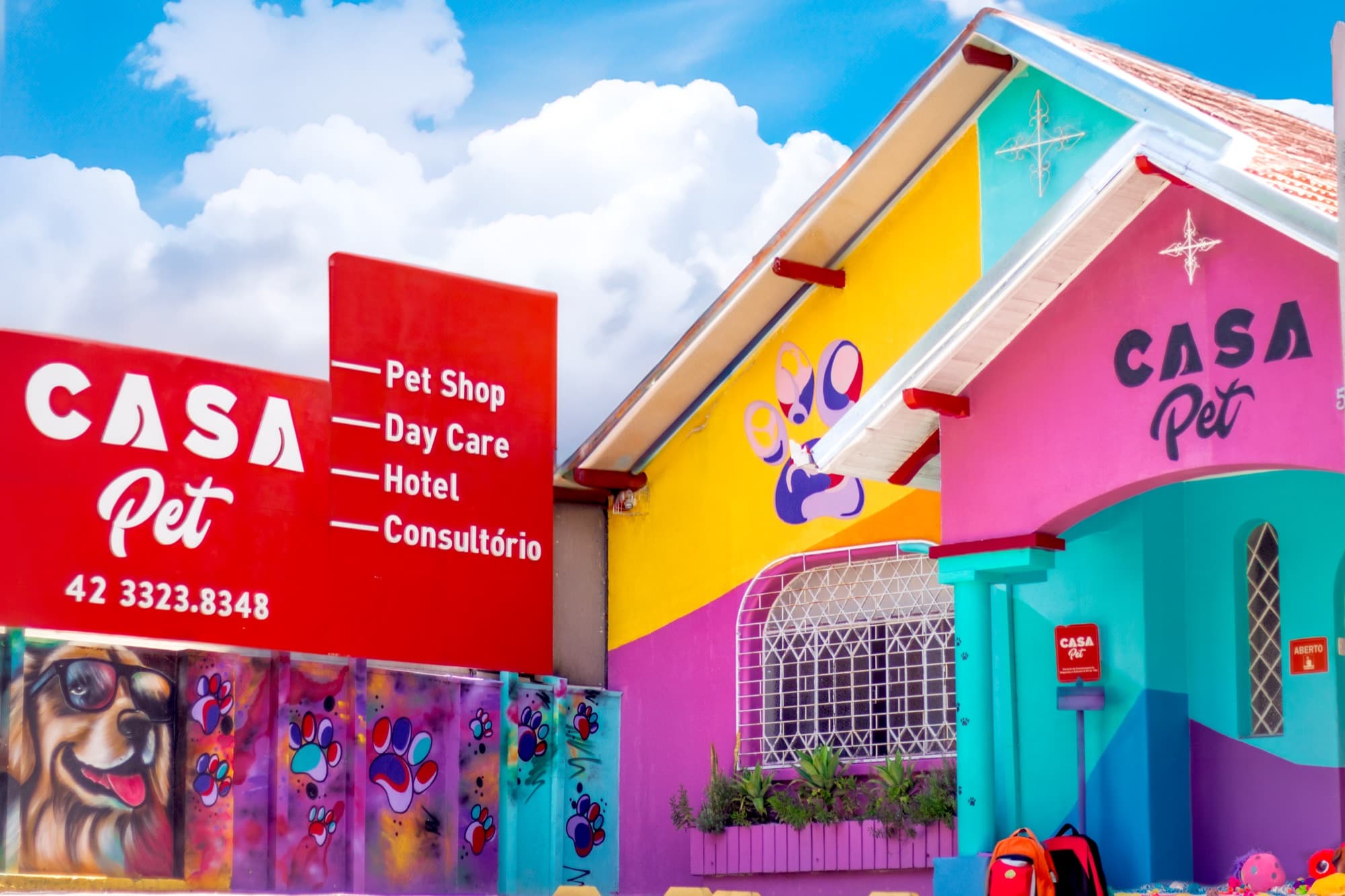 Fachada da Casa Pet em Ponta Grossa: casinhas pintadas de rosa, amarelo e turquesa com o letreiro e a placa de serviços