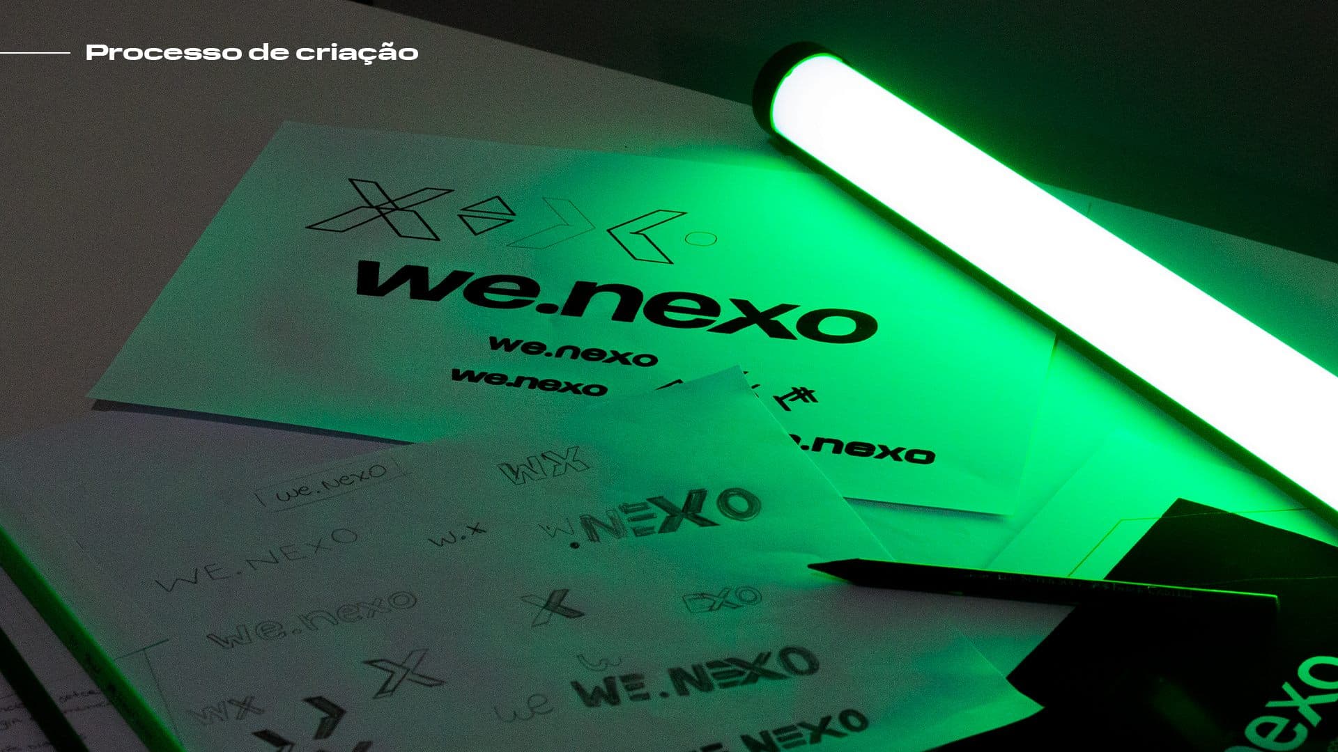 Papéis com variações do logo we.nexo iluminados por bastão de luz LED verde